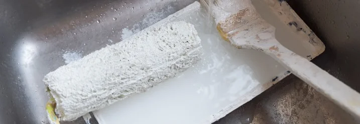 Farbroller und Pinsel werden in einem Waschbecken gereinigt.